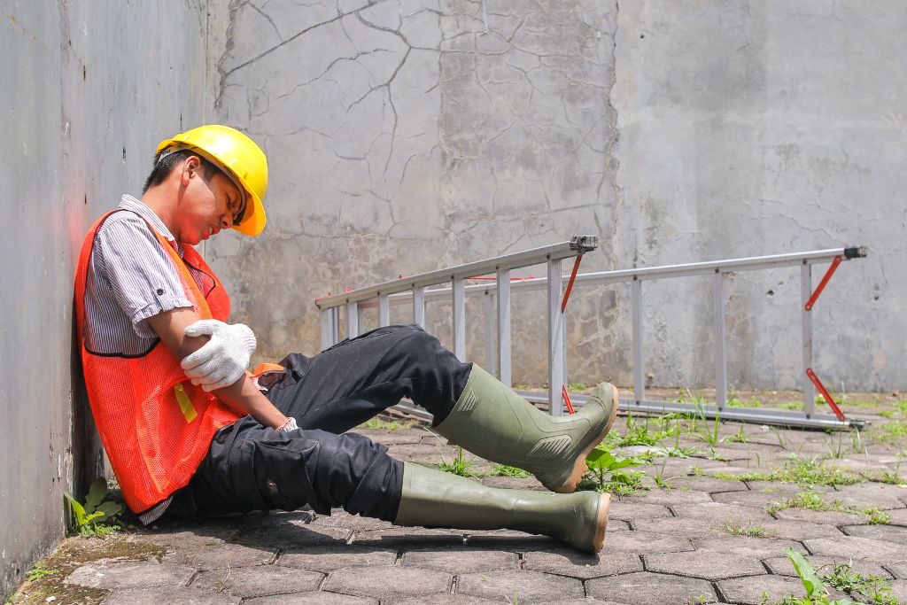 Injured construction worker sitting near a job site ladder, representing workplace accident risks tied to safety and compliance policies.