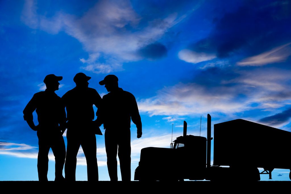 Silhouette of three commercial truck drivers in front of a semi-truck at sunset, symbolizing Idaho employers reducing workers’ comp risks with proactive drug testing programs.