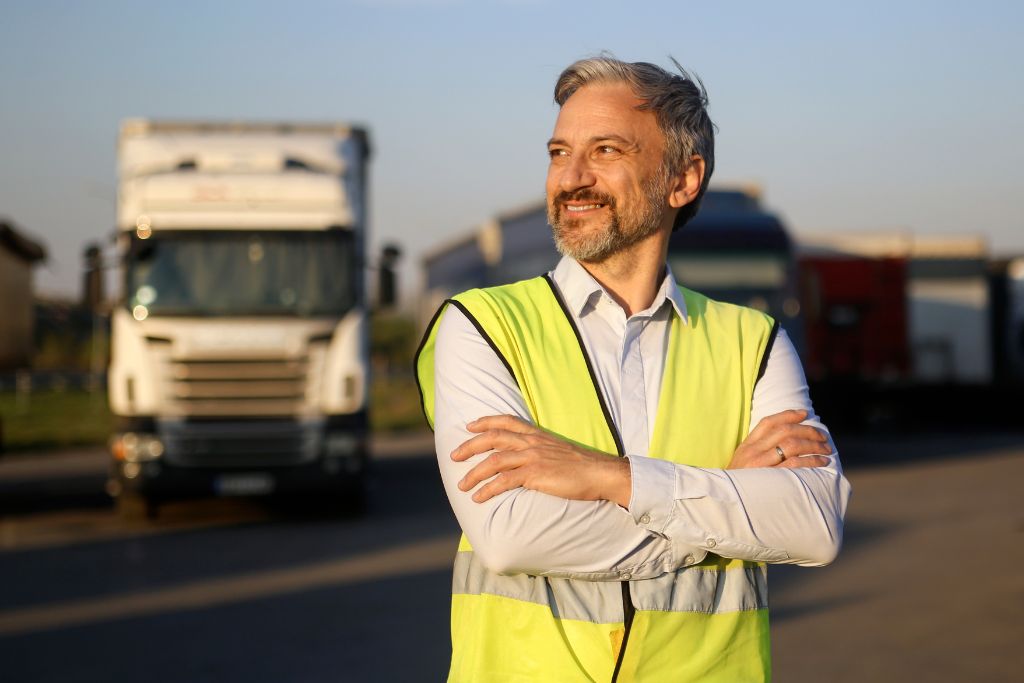 Confident safety manager in a reflective vest standing in front of trucks, representing effective reasonable suspicion documentation in transportation workplaces.