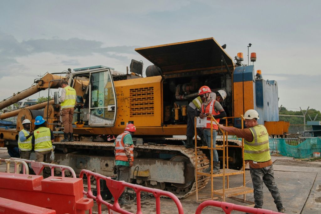 Idaho construction workers collaborating around heavy equipment while following drug testing and safety protocols to reduce workers’ comp risks.